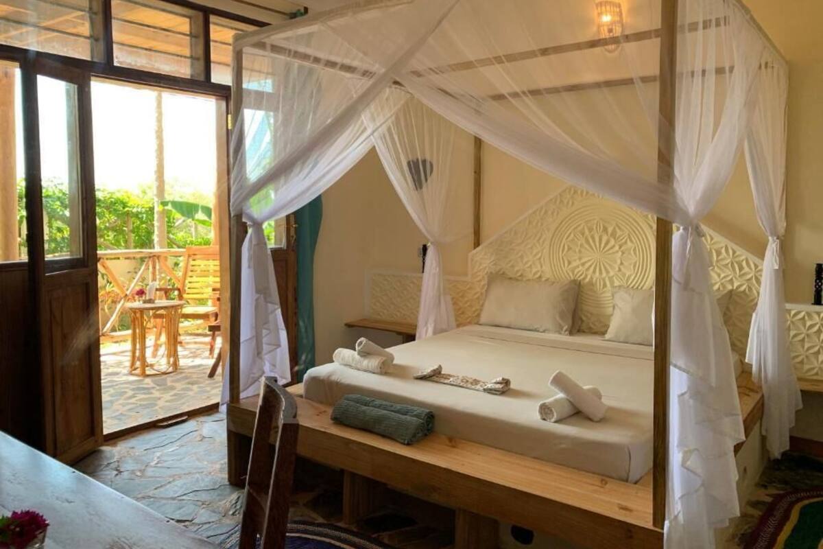 Ein Zimmer mit Himmelbett, einer Holzbank und Blick ins Freie.