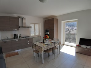 A modern kitchen with a dining area, a large window with a view, and a TV in a corner. - Apartment Ninfea with beatiful lake view (Veneto)