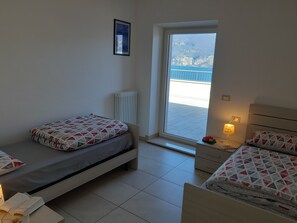 A bedroom with two beds, a radiator, a window with a view of mountains, and a bedside table with a lamp. - Apartment Ninfea with beatiful lake view (Veneto)
