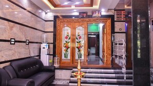 A lobby with a black leather sofa, a water dispenser, a decorative mirror, and a sign indicating room numbers. - MGM Suite Rooms (Tiruvannamalai)