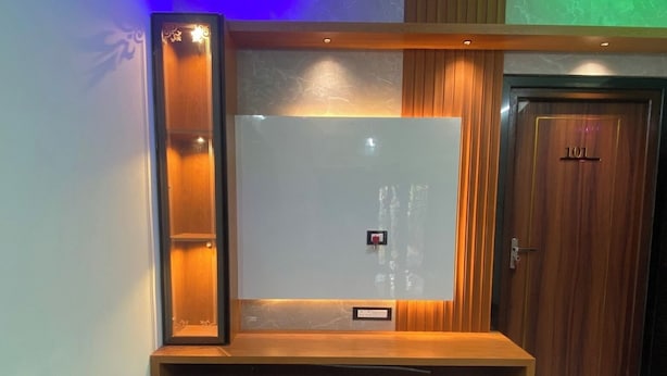 A modern suite room with a large flat-screen TV mounted on a wooden console with drawers. - MGM Suite Rooms (Tiruvannamalai)