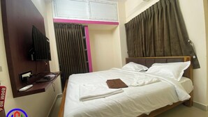 A hotel room with a bed, a TV mounted on the wall, an air conditioning unit, and a window with curtains. - MGM Suite Rooms (Tiruvannamalai)