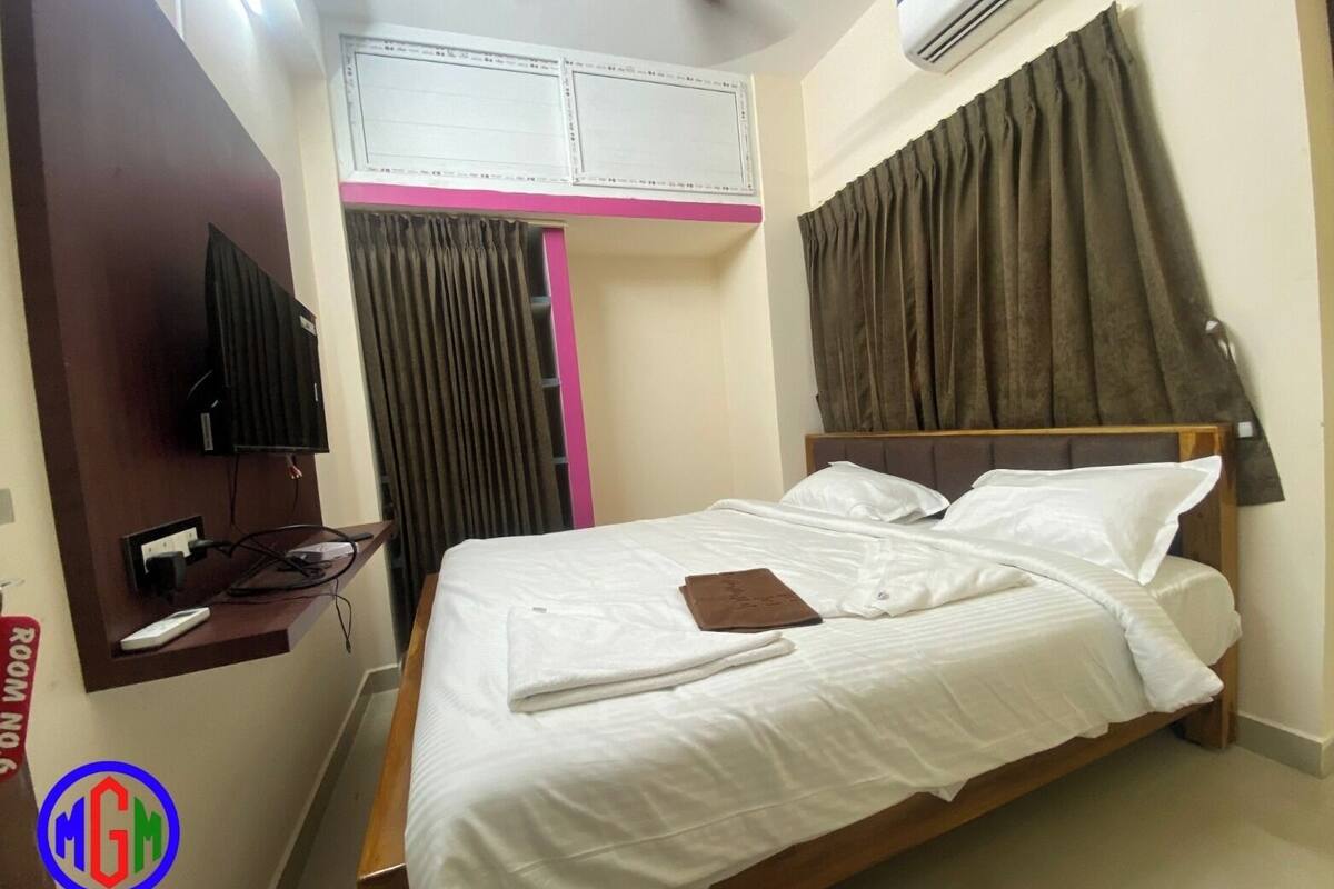 A hotel room with a bed, a TV mounted on the wall, an air conditioning unit, and a window with curtains.