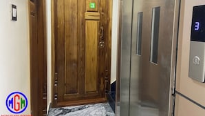 A wooden door with a green number plate, an elevator with a digital display, and a marble floor. - MGM Suite Rooms (Tiruvannamalai)