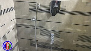 A shower area with a handheld showerhead and a wall-mounted control. - MGM Suite Rooms (Tiruvannamalai)