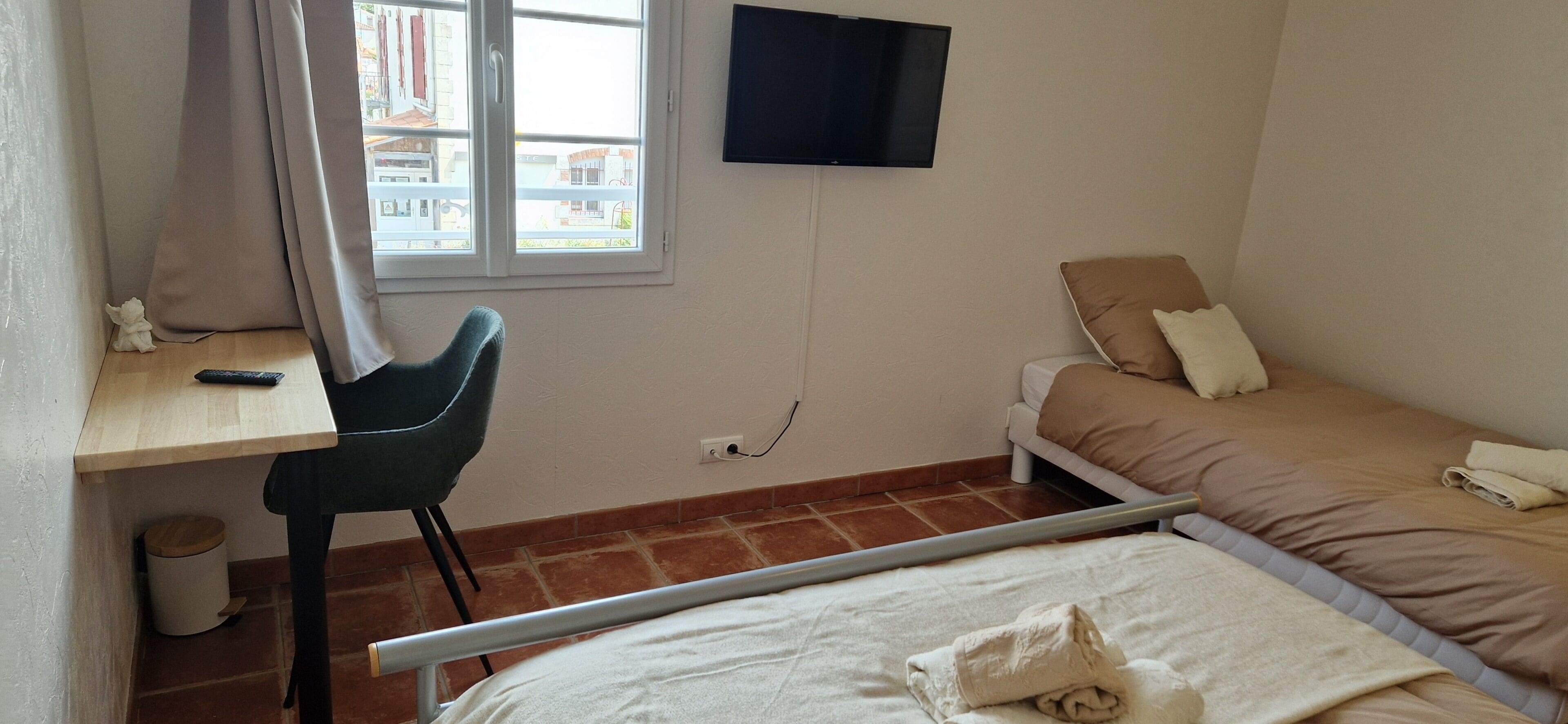Ein Schlafzimmer mit einem Bett, einem Schreibtisch mit Stuhl, einem an der Wand befestigten Fernseher und einem Fenster mit Vorhängen.