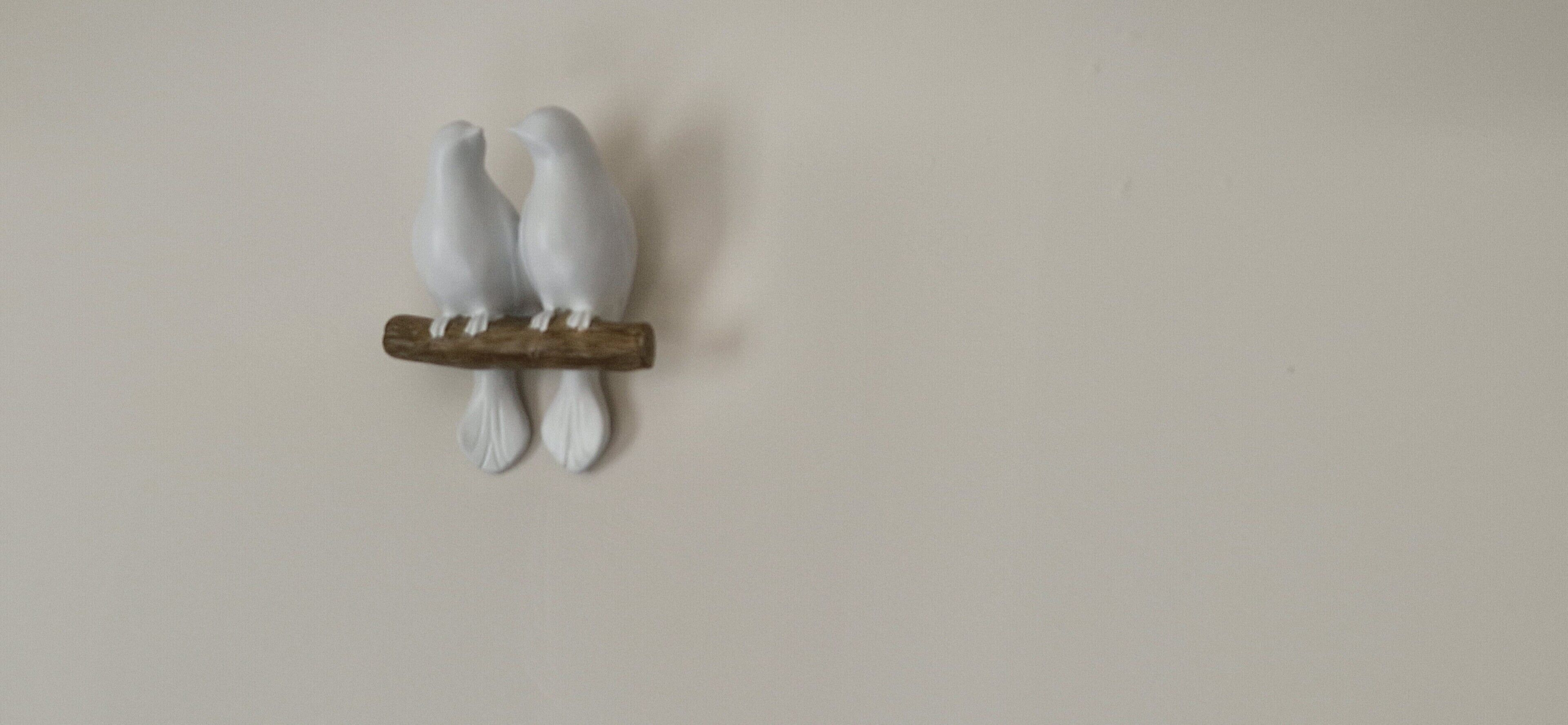 Una scultura a parete raffigurante due uccelli bianchi appollaiati su un ramo.
