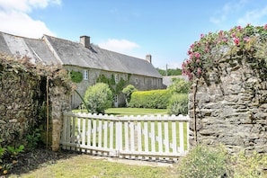 A stone building with a white fence, a garden, and a clear sky.