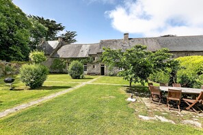 A stone building with a grassy yard, a wooden table, and chairs.