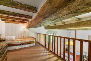 A room with exposed wooden beams, a bed, a desk, and a window with a view.