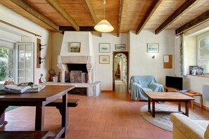 Ein rustikales Interieur mit Kamin, Holzbalken, einem Esstisch und einem Fernseher.