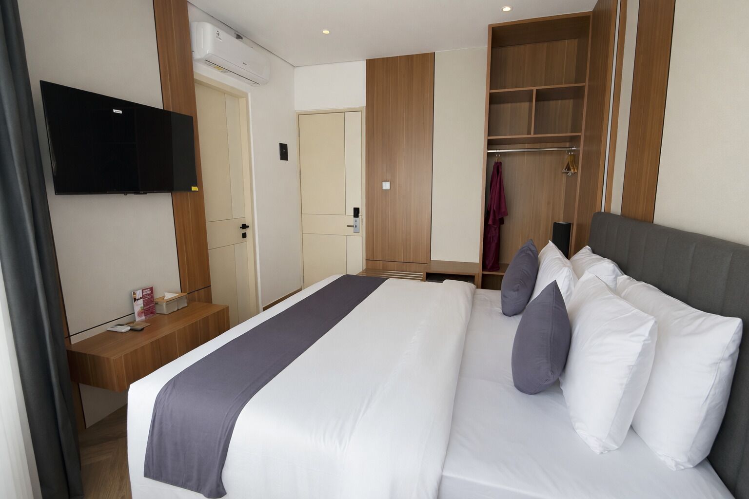A hotel room with a large bed, a TV mounted on the wall, a wooden wardrobe, and a coat rack.