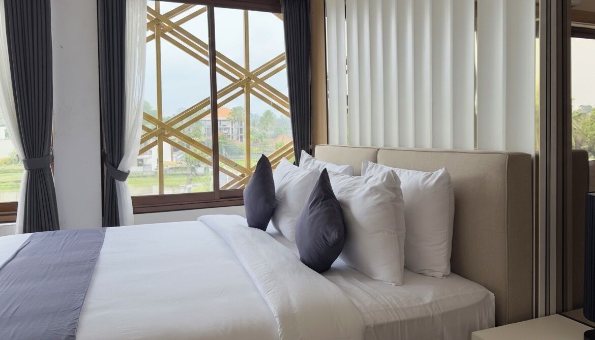 A hotel room with a large bed, a view through a window with a geometric design, and a curtain on the left.