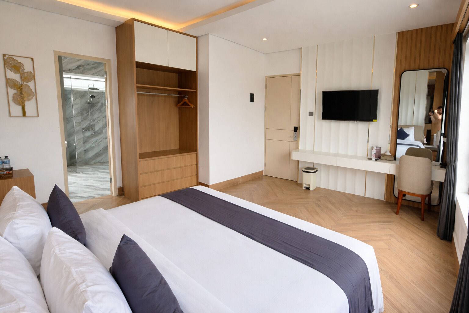 Een hotelkamer met een groot bed, een kledingkast, een bureau met stoel, een televisie en een douche.