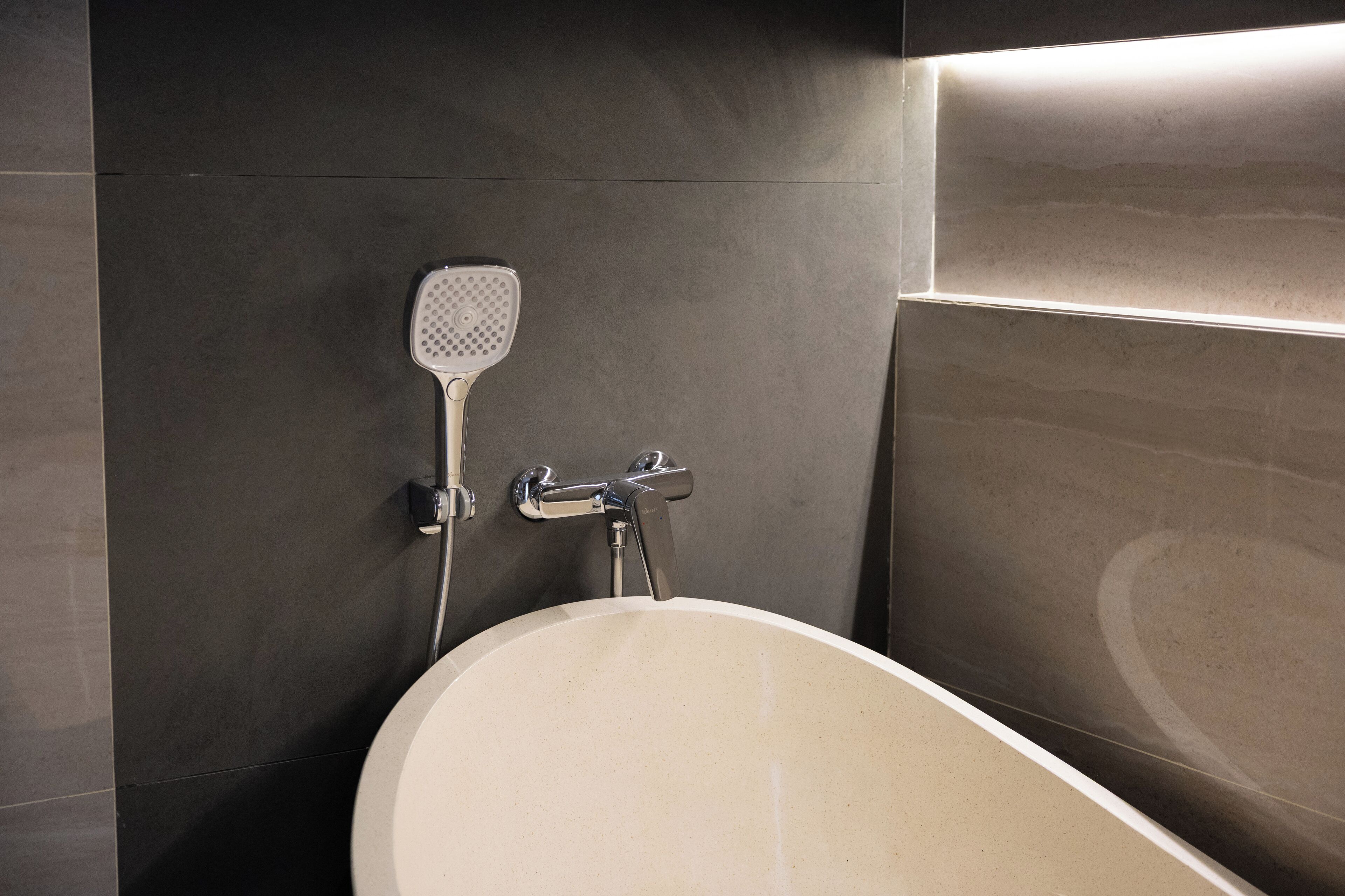 A modern bathroom with a freestanding bathtub, a handheld showerhead, and a wall-mounted faucet.