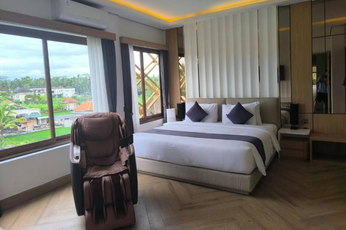A modern hotel room with a large bed, a massage chair, and a view of the city.