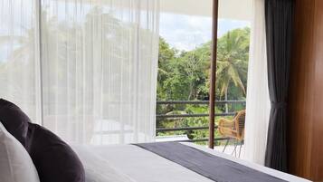 A hotel room with a bed, a window with sheer curtains, and a view of greenery outside.