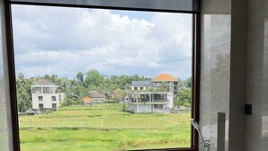 A modern bathroom with a freestanding bathtub, a large window, and a view of a residential area. - Rendezvous Wellness & Resort (Ubud)
