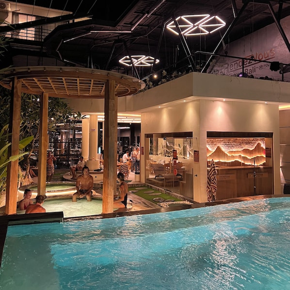 A pool area with a covered seating area, a bar, and a view of the cityscape. - Rendezvous Wellness & Resort (Ubud)