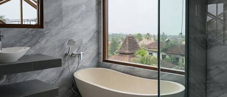 A modern bathroom with a freestanding bathtub, a large window offering a view of buildings, and a marble-tiled wall.