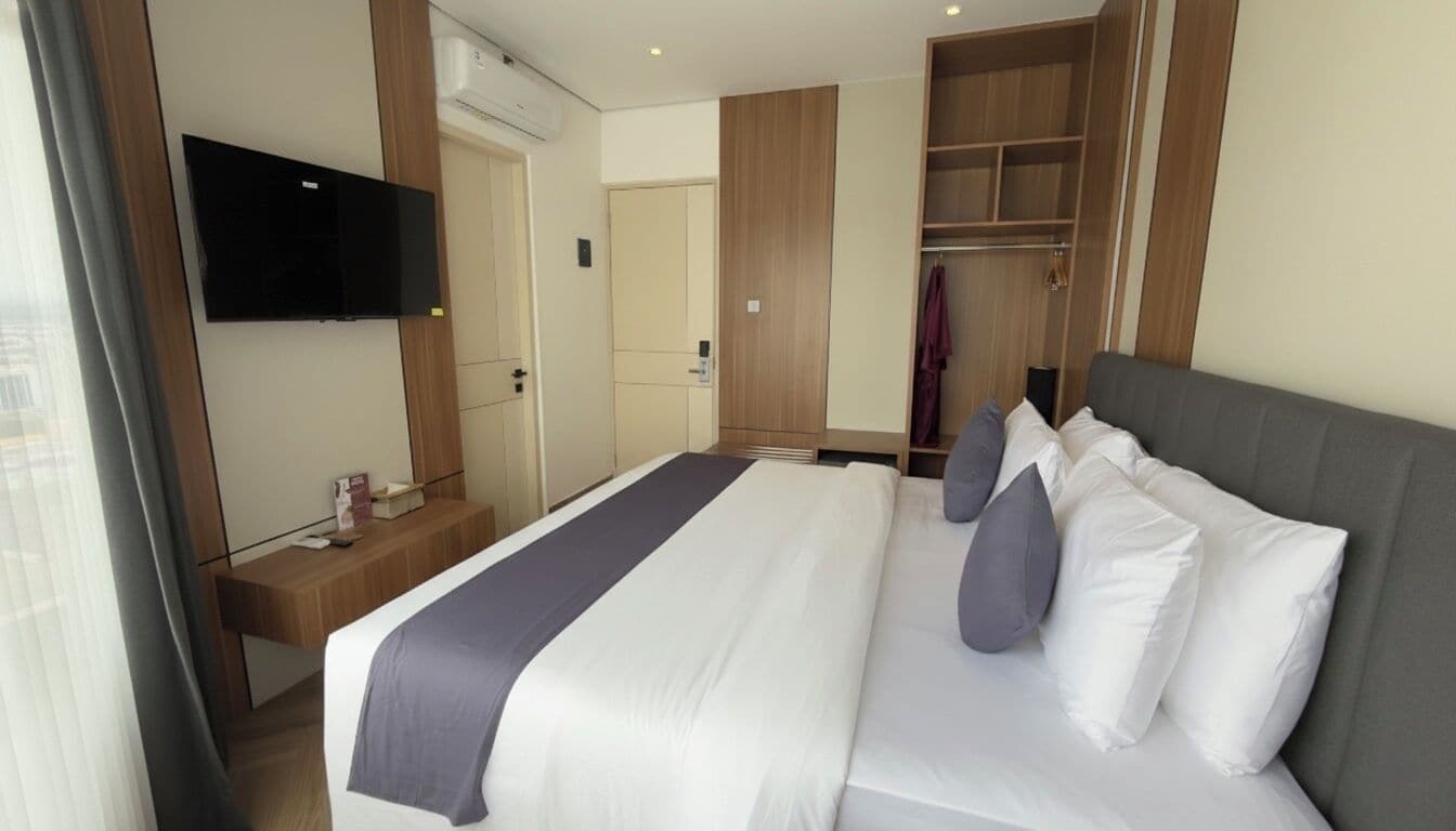A hotel room with a large bed, a TV mounted on the wall, a wardrobe, and a bedside table.