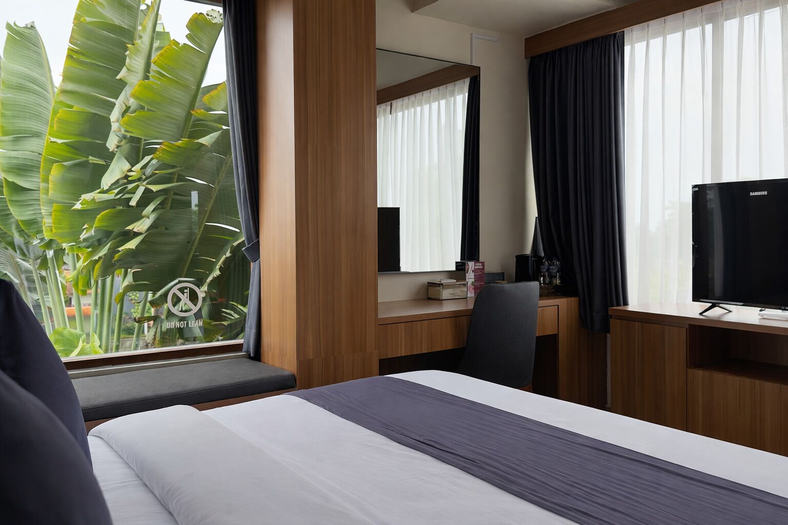 Une chambre d’hôtel avec un lit, un bureau, une chaise, une télévision et une fenêtre avec des rideaux.