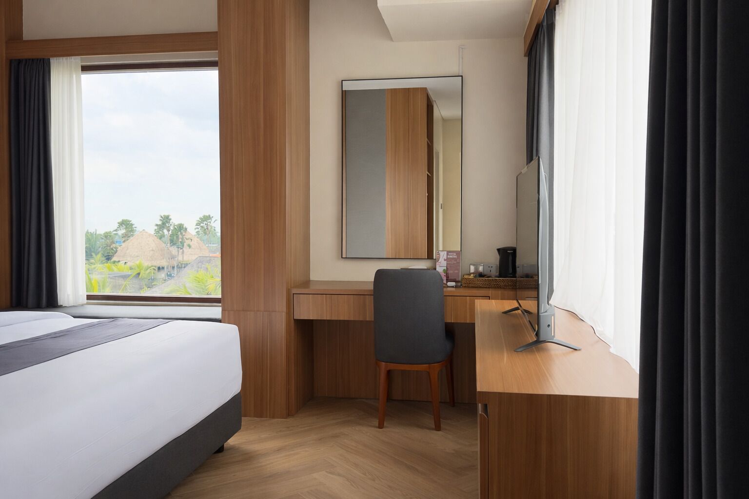 A hotel room with a bed, a desk, a chair, a large mirror, and a view of the outdoors.