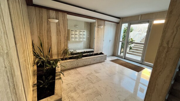 A spacious lobby with marble flooring, a built-in planter with plants, a reception desk, and a view of the outside through large sliding doors.