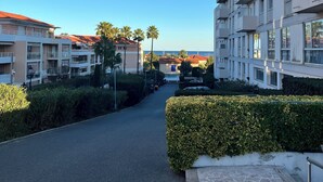 A pathway leading to a modern building with balconies and a clear view of the sea.
