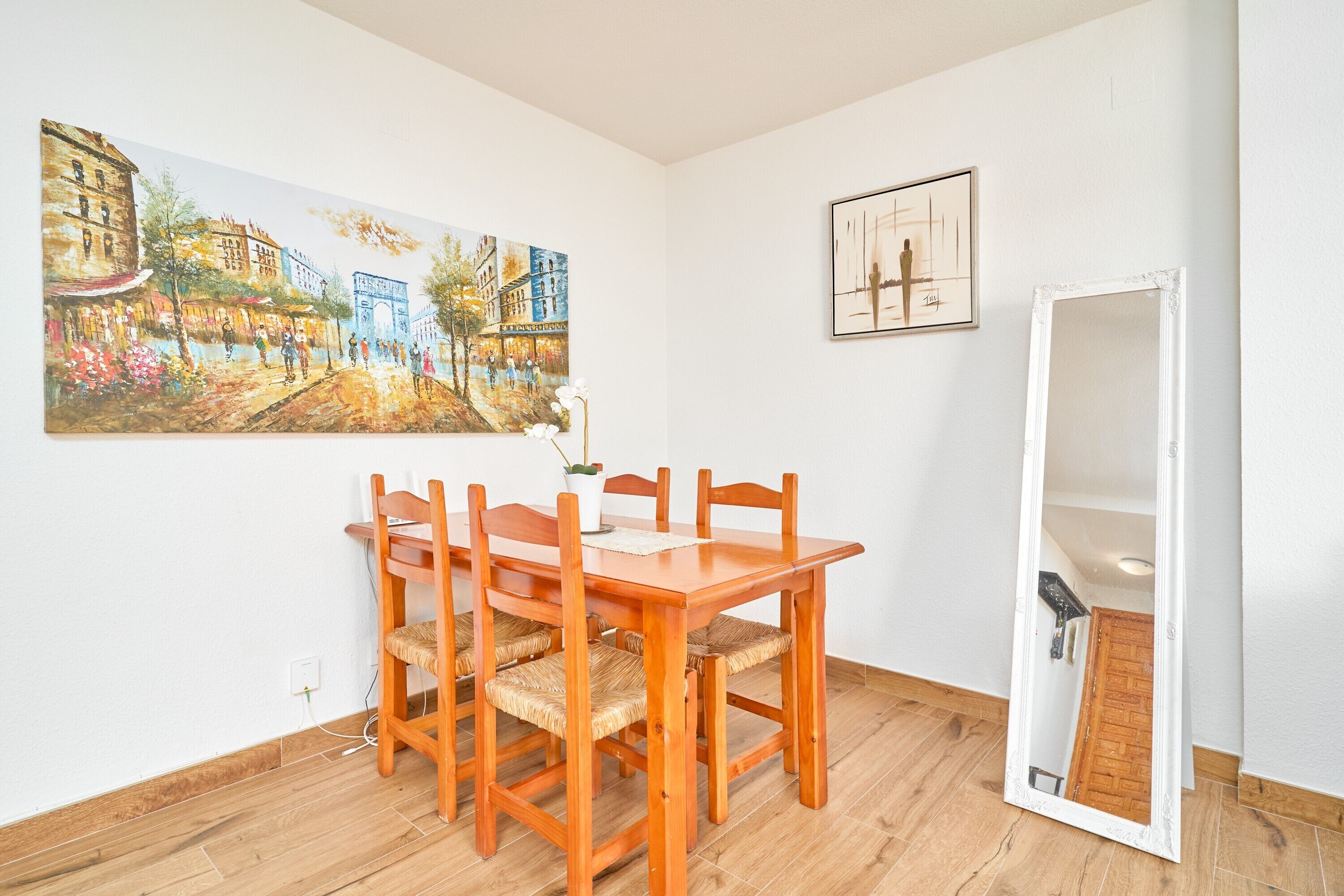 A dining area with a wooden table and chairs, a painting on the wall, and a mirror.