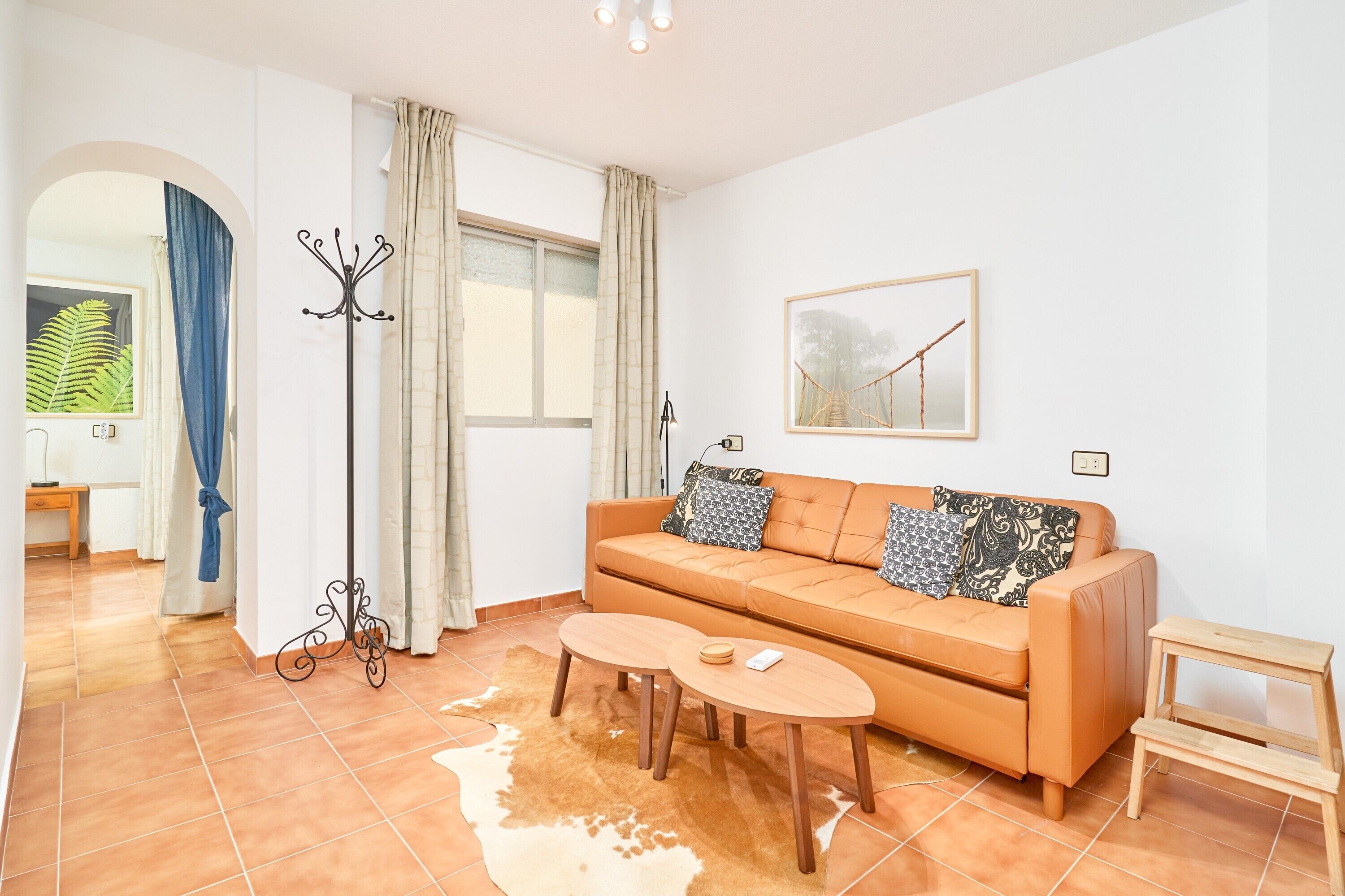 Ein Wohnzimmer mit einer Couch, zwei Couchtischen, einem Kleiderständer und einem gerahmten Bild an der Wand.