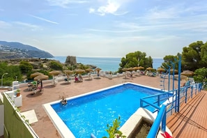 Une piscine avec vue sur la mer, des parasols et des chaises longues.