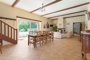 A spacious dining area with a wooden table and chairs, a staircase, and a view of greenery outside.
