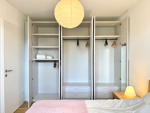 A bedroom with a bed, a wardrobe with open doors, and a bedside lamp. - 70m2 Apartment near Kirschblütenpark - UNO-City - Vienna International School (Wien)