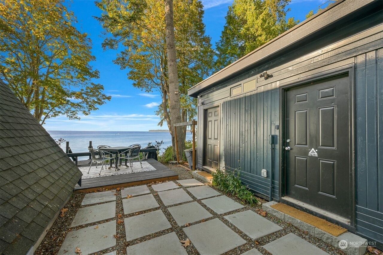 Une terrasse dallée de pierres, une table et des chaises, et une vue sur la mer.