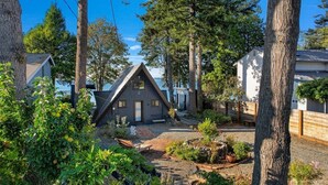 Una cabaña de techo triangular rodeada de árboles y un camino de grava.