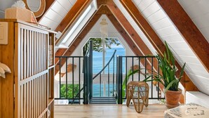 Habitación de ático con techos altos y una escalera de madera que da a un balcón con vistas al mar.