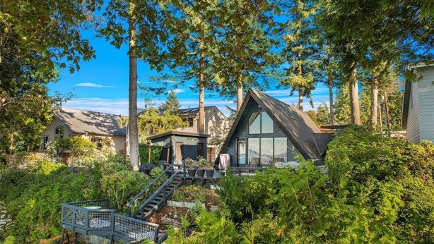 Una casa moderna con un amplio ventanal de vidrio, rodeada de exuberante vegetación y altos árboles.