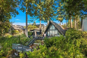 Una casa moderna con un'ampia vetrata, immersa nel verde e circondata da alberi alti.