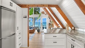 Una cocina con armarios blancos, un refrigerador de acero inoxidable y techo de madera.