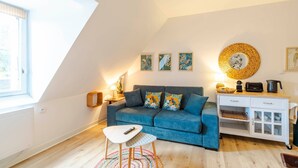 Una sala de estar acogedora con un sofá azul, una mesita blanca, un mueble blanco y un ventanal grande.