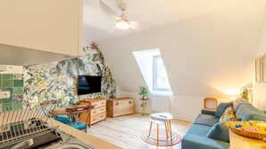 Una cocina moderna con televisor integrado, un comedor con mesa y sillas de madera, una zona de estar acogedora con sofá y un amplio ventanal que aporta luz natural.