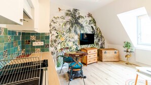 Una habitación con pared de azulejos, televisión, mesa de comedor con sillas, cómoda y ventana.