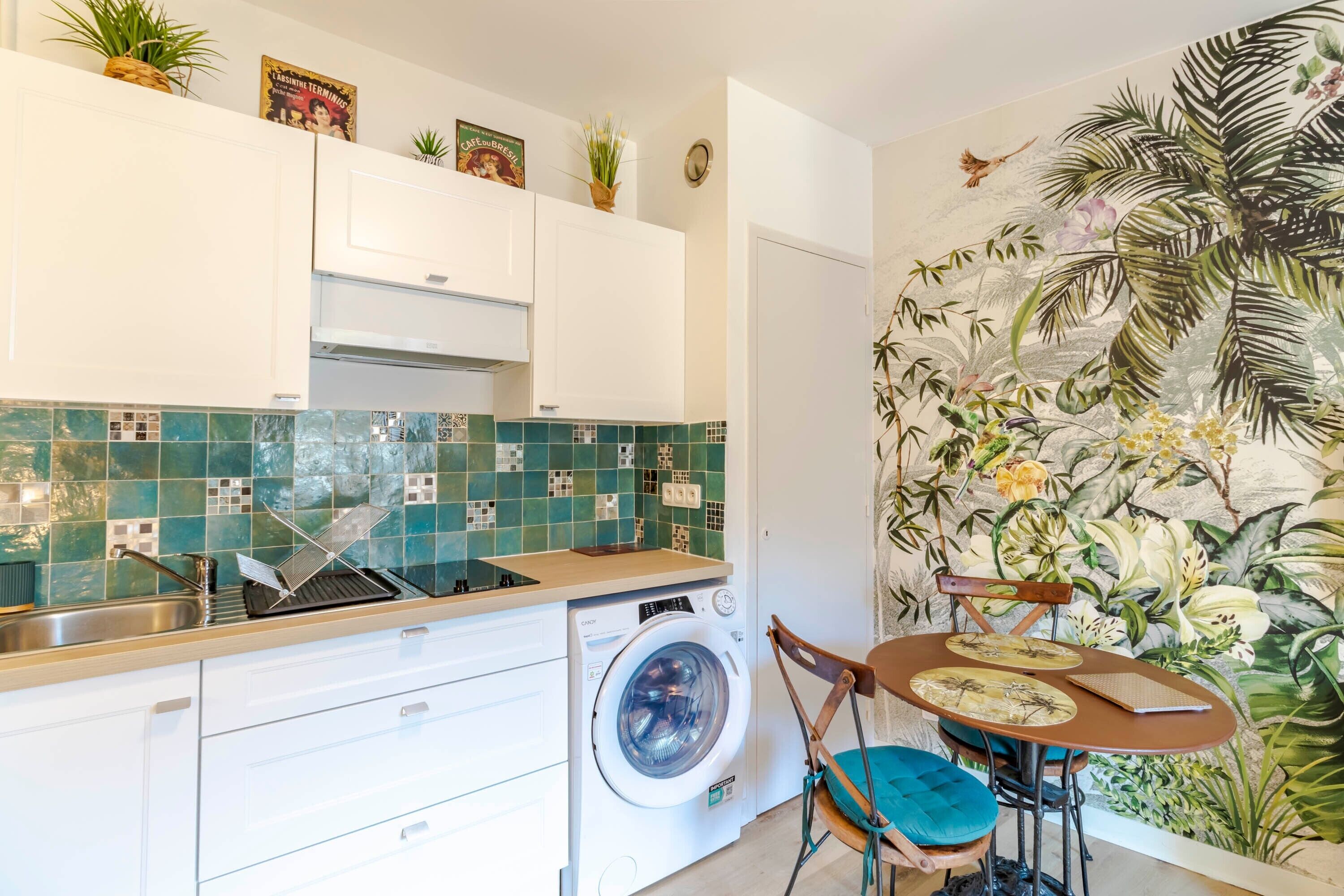 Une cuisine compacte équipée d’un lave-linge, d’un évier et d’un coin repas avec une table et des chaises.