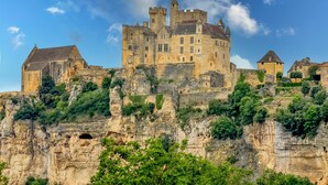 Un castillo histórico con múltiples torres, ubicado en un acantilado con abundante vegetación.