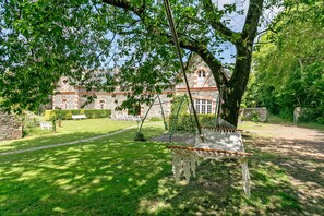 A hammock under a tree in a garden with a stone building in the background.