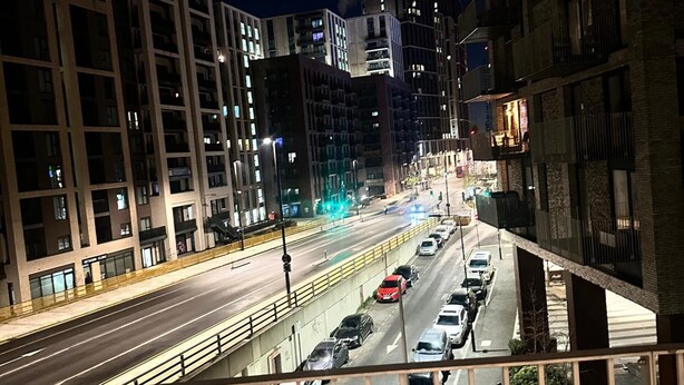 A nighttime cityscape with a multi-lane road, buildings with illuminated windows, and a pedestrian walkway. - Luxury two bed two Bath In Excel (London)