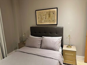 Une chambre à coucher comprenant un lit, une tête de lit, une table de chevet avec une lampe et une petite table de nuit avec un récipient en verre.