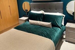 A neatly made bed with a teal and beige duvet, a grey headboard, and a bedside table with a lamp. - Luxury two bed two Bath In Excel (London)