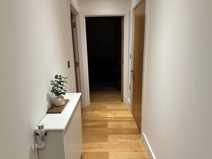 Un couloir étroit avec un plancher en bois, des murs blancs et un radiateur blanc sur le côté gauche.